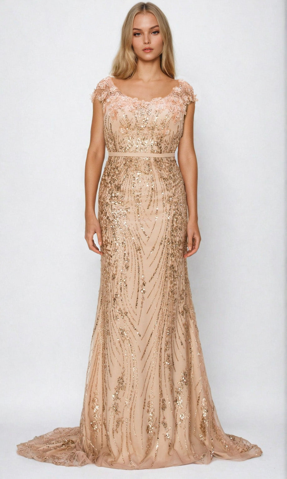 A woman stands wearing the Cinderella Couture 8057J, a floor-length fitted blush prom dress with gold sequins, beading, cap sleeves, and a sheer neckline.